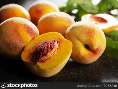 Peaches with leaves on dark table with peach in halves with peach seed stone.