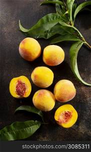 Peaches with leaves on dark table with peach in halves with peach seed stone.
