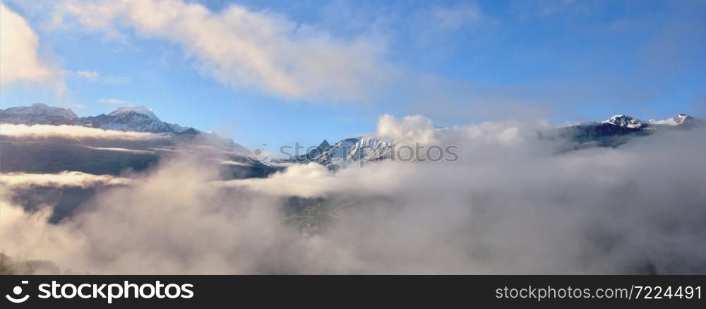 peak of mountain range emerging of white clouds in alps in blue sky