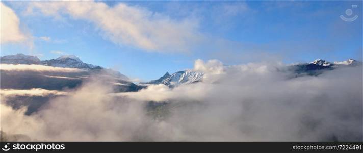 peak of mountain range emerging of white clouds in alps in blue sky
