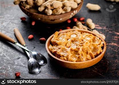 Peanut butter and inshell peanuts in wooden plates. On a rustic dark background. High quality photo. Peanut butter and inshell peanuts in wooden plates.