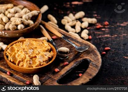 Peanut butter and inshell peanuts in wooden plates. On a rustic dark background. High quality photo. Peanut butter and inshell peanuts in wooden plates.