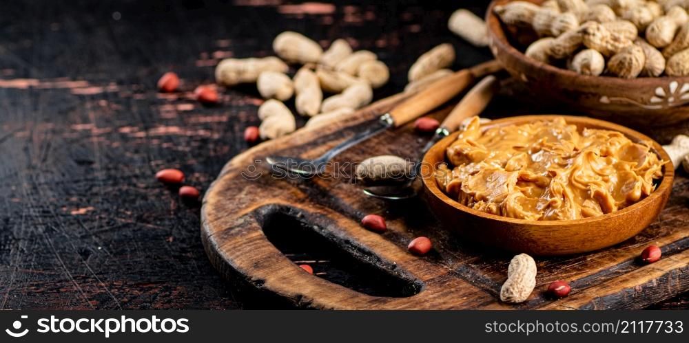 Peanut butter and inshell peanuts on a cutting board. Against a dark background. High quality photo. Peanut butter and inshell peanuts on a cutting board.
