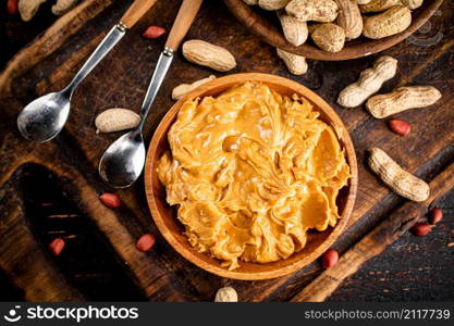 Peanut butter and inshell peanuts on a cutting board. Against a dark background. High quality photo. Peanut butter and inshell peanuts on a cutting board.