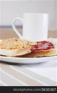 Peanut butter and jam on slices of bread with cup of coffee