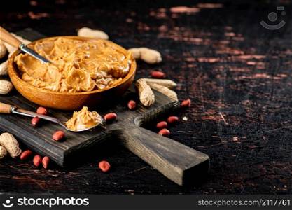 Peanut butter in a spoon on a cutting board. Against a dark background. High quality photo. Peanut butter in a spoon on a cutting board.