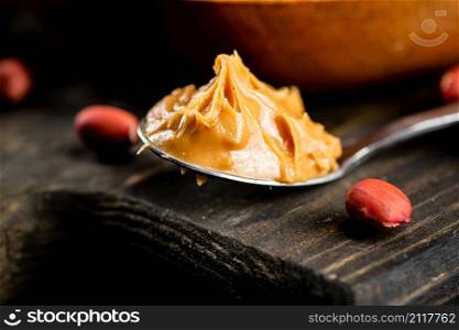Peanut butter in a spoon on a cutting board. Against a dark background. High quality photo. Peanut butter in a spoon on a cutting board.