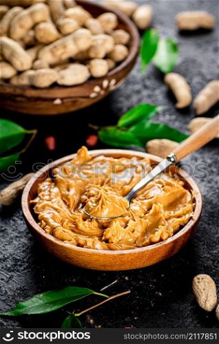 Peanut butter in a wooden plate. On a black background. High quality photo. Peanut butter in a wooden plate.