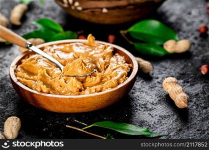 Peanut butter in a wooden plate. On a black background. High quality photo. Peanut butter in a wooden plate.