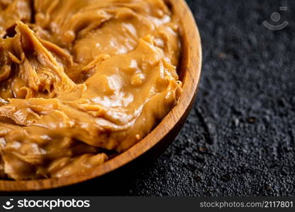 Peanut butter in a wooden plate on the table. On a black background. High quality photo. Peanut butter in a wooden plate on the table.
