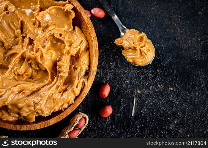 Peanut butter in a wooden plate on the table. On a black background. High quality photo. Peanut butter in a wooden plate on the table.