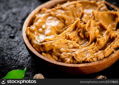 Peanut butter in a wooden plate on the table. On a black background. High quality photo. Peanut butter in a wooden plate on the table.