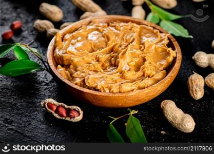 Peanut butter in a wooden plate on the table. On a black background. High quality photo. Peanut butter in a wooden plate on the table.