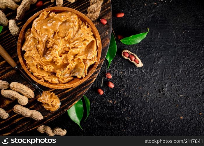 Peanut butter on a wooden tray with leaves. On a black background. High quality photo. Peanut butter on a wooden tray with leaves.