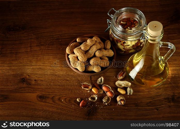 Peanut oil in bottle and dry nuts on wooden table. Top view. Free space for text.