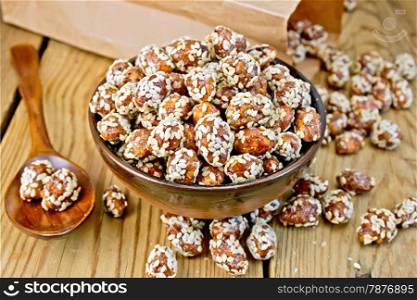 Peanut sweet caramel with sesame seeds in a bowl and a spoon, napkin, paper bag on a wooden boards background