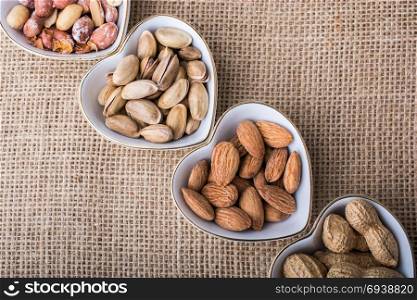 Peanuts, almonds, pistachio in heart shaped plates on canvas