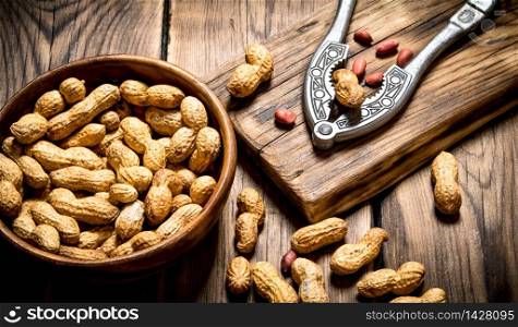 Peanuts in a bowl with a Nutcracker on the Board. On wooden background.. Peanuts in a bowl