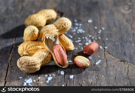 Peanuts in shells and salt on wood background