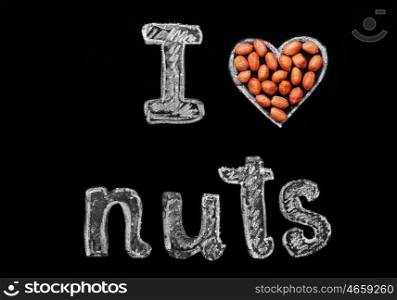 "Peanuts on a black background and chalk inscription "I love nuts". Heart drawn in chalk and peanuts."