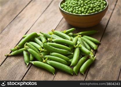 Peapods (lat. Pisum sativum) on table with a bowl of peas in the back (Selective Focus, Focus into the middle of the peapods)