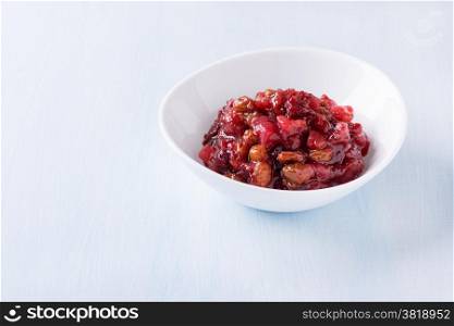 Pear cranberry relish for Christmas in a white bowl over light blue background with copy space