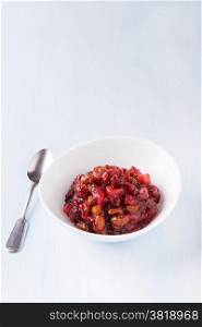 Pear cranberry relish for Christmas in a white bowl over light blue background with copy space