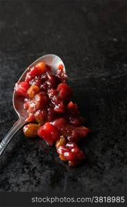 Pear cranberry relish in spoon over dark background, copy space, selective focus