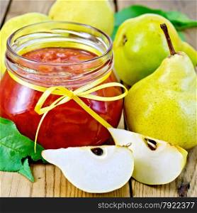 Pear jam in a glass jar, yellow pears, green leaves on a wooden boards background