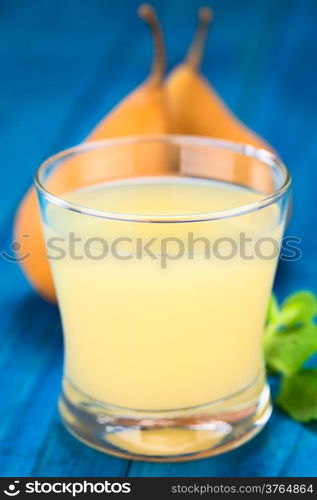 Pear juice in glass with Bosc pear in the back on blue wood (Selective Focus, Focus on the front rim of the glass)