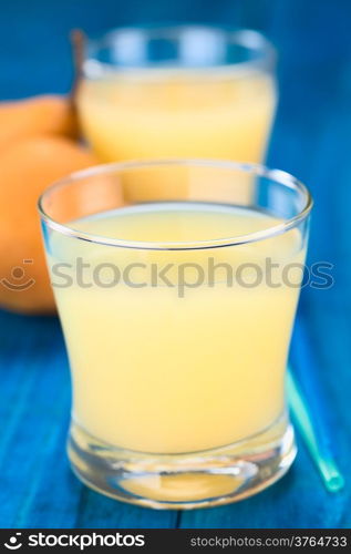 Pear juice in glass with drinking straws on the side and Bosc pear in the back on blue wood (Selective Focus, Focus on the front rim of the glass)