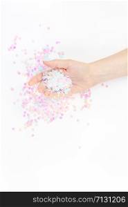 Pearl pastel confetti sparkles with woman hand on white background. Creative conceptual top view flat lay backdrop for your blog, text or design