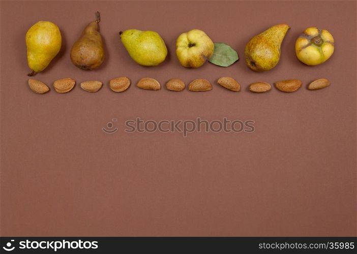 Pears and quince in shell almonds in row on yellow background with copy space