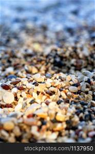 Pebble beach on the sea coast is illuminated by a narrow sunbeam and plays with colorful colors, the foreground and background are blurred, close-up, vertical image with copy space.. Beach pebbles backlit by a bright sunbeam.