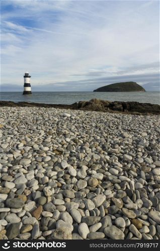 Pebbled beach looking to small lighthouse and island. Penmon, Anglesey, Wales, United Kingdom.