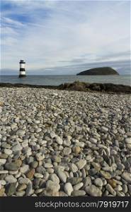 Pebbled beach looking to small lighthouse and island. Penmon, Anglesey, Wales, United Kingdom.