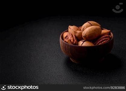 Pecan nuts in shell and peeled in a wooden round bowl on a dark concrete background