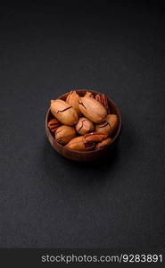 Pecan nuts in shell and peeled in a wooden round bowl on a dark concrete background