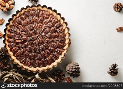 Pecan pie, tart in a baking dish on a white table. Flat lay traditional holiday dessert for Thanksgiving or Christmas holidays. View from above with copy space