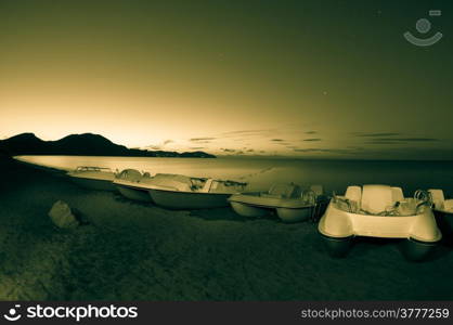 Pedal boats on the sea beach at night. Toned.
