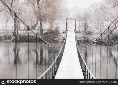 Pedestrian suspension bridge made of steel and wood across the river, winter.. Pedestrian suspension bridge made of steel and wood across the river, winter