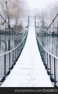 Pedestrian suspension bridge made of steel and wood across the river, winter.. Pedestrian suspension bridge made of steel and wood across the river, winter