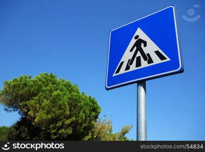 Pedestrian symbol on road sign close to a park during a beautiful day with blue sky.