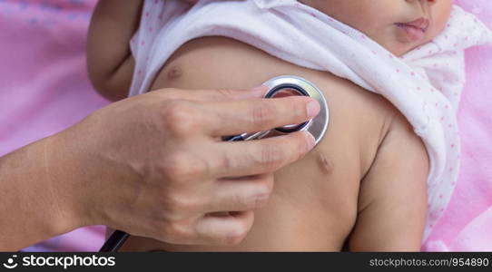 Pediatric doctor exams newborn baby girl with stethoscope in hospital.