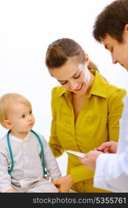 Pediatric doctor explaining something to mother while baby playing on table&#xA;