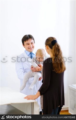 Pediatric doctor holding baby and talking with mother&#xA;