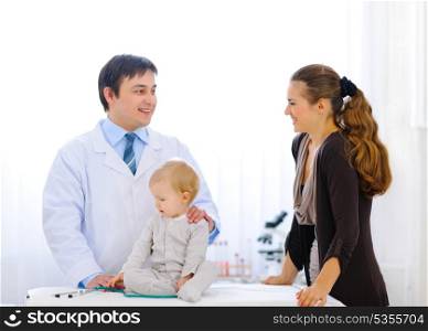 Pediatric doctor talking with mother while baby playing with stethoscope &#xA;