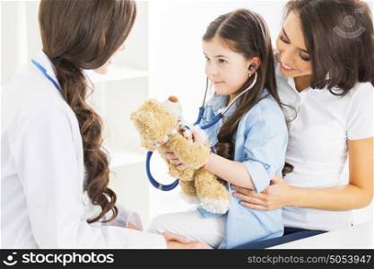 Pediatrician and family. Mother and daughter at pediatrician office, girl examinate heart beat of teddy bear with stethoscope