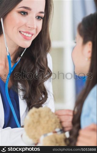 Pediatrician and girl. Beautiful female pediatrician doctor examining child with teddy bear in office