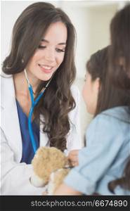 Pediatrician and girl. Beautiful female pediatrician doctor examining child with teddy bear in office